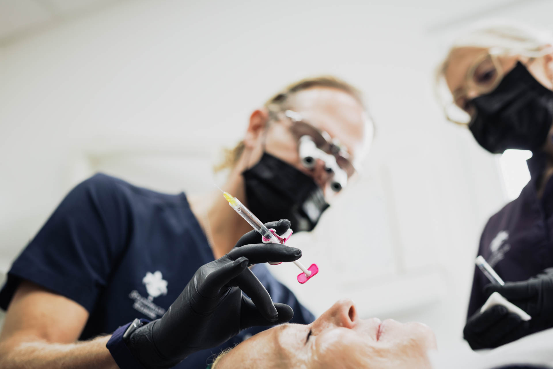 Nahaufnahme einer Injektionsbehandlung mit zwei Behandlern in der Stadtwald Klinik